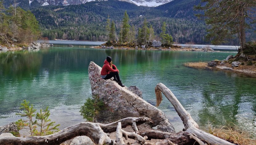 Frau sitzt auf Stein am Eibsee und schaut auf den See im Frühjahr