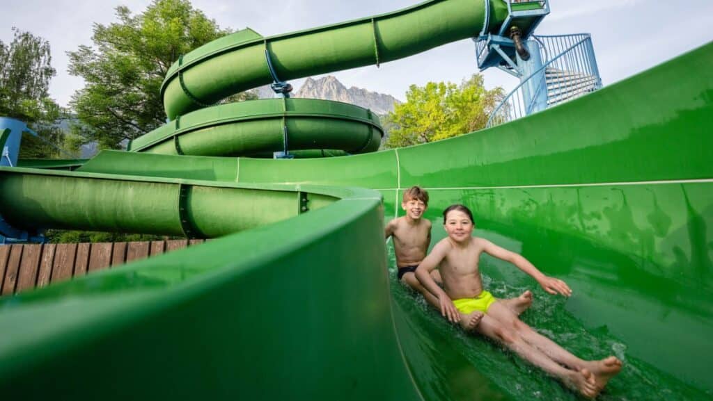 Zwei Jungen in der Wasserrutsch im Grainauer Freibad im Hintergrund Bergspitzen