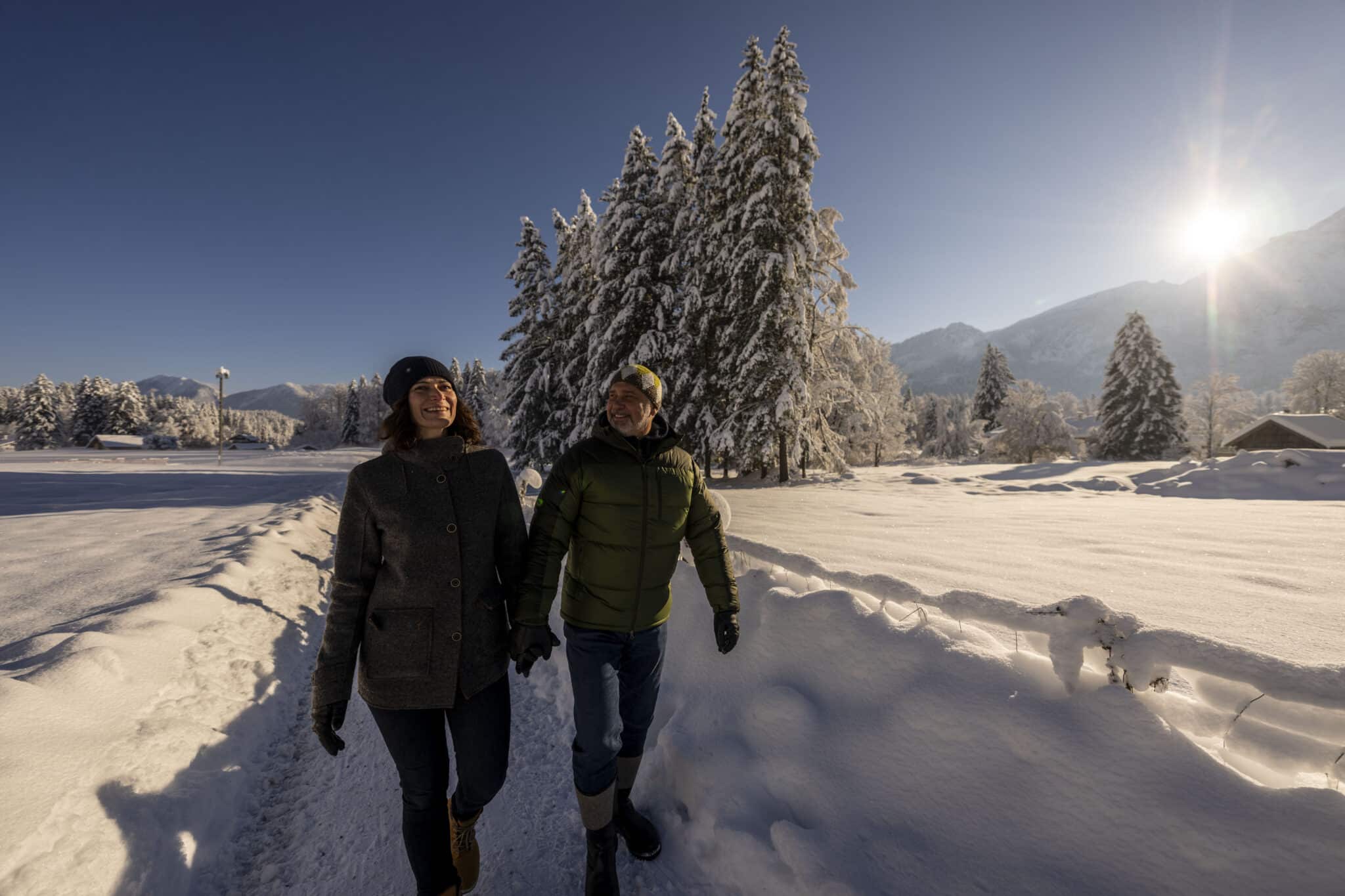 Paar spaziert durch sonnige Winterlandschaft in Grainau