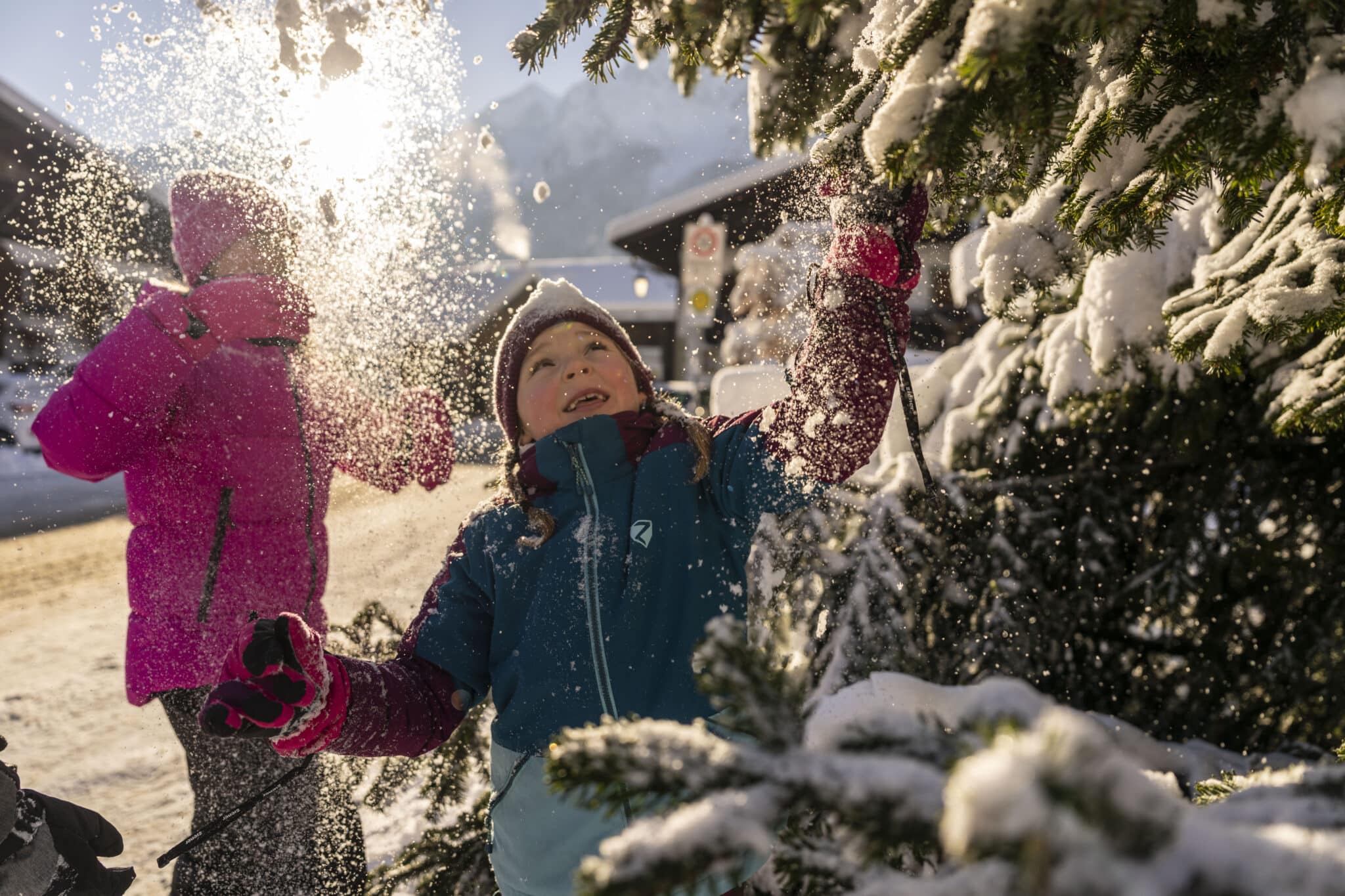 Strahlendes Mädchen am Unteren Dorfplatz in Grainau das mit Schnee auf Baum wirft der in der Sonne glitzert