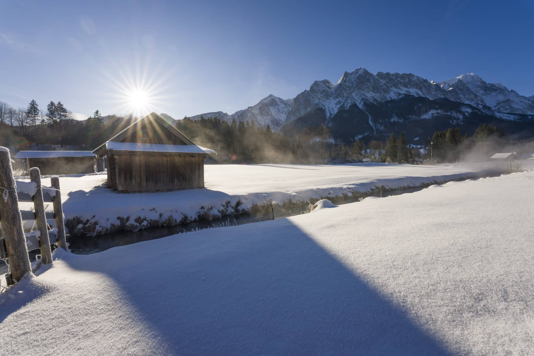 Verschneiter Krepbach mit Heustadel und Sonne mit Strahlen dahinter Waxensteine, Alpspitze und Zugspitze
