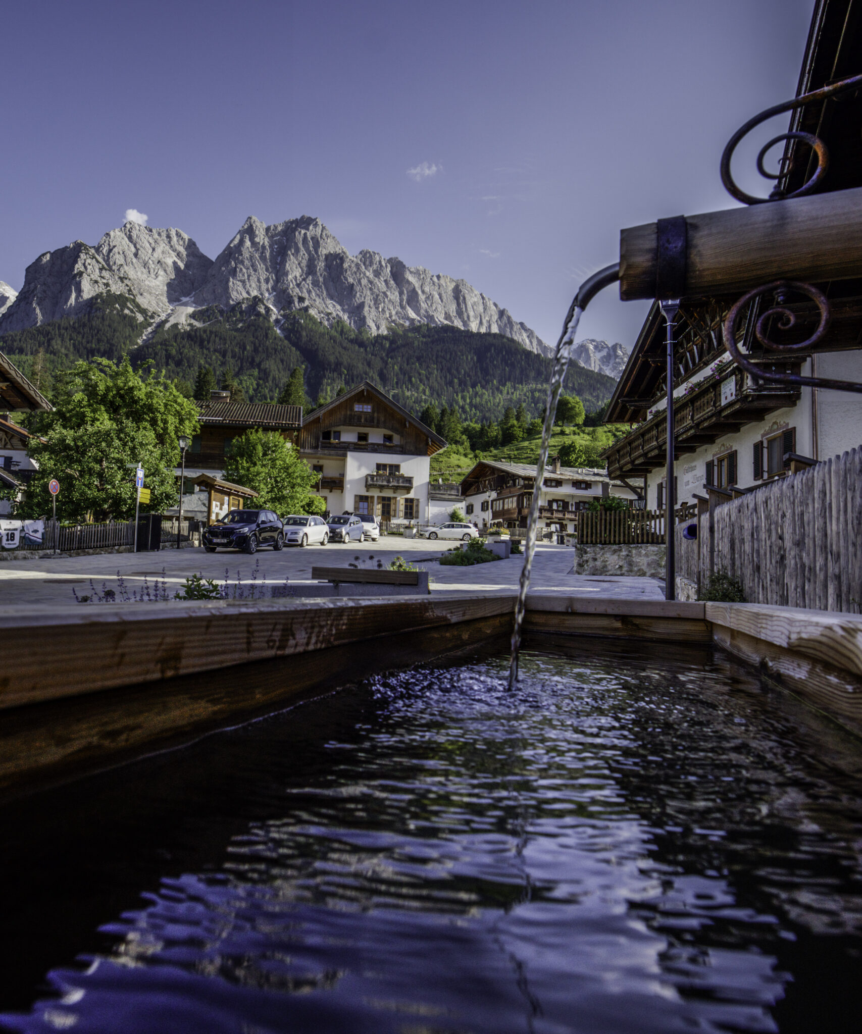 Oberer Dorfplatz in Grainau im Hintergrund Waxensteine und Zugspitze mit Brunnen im Vordergrund