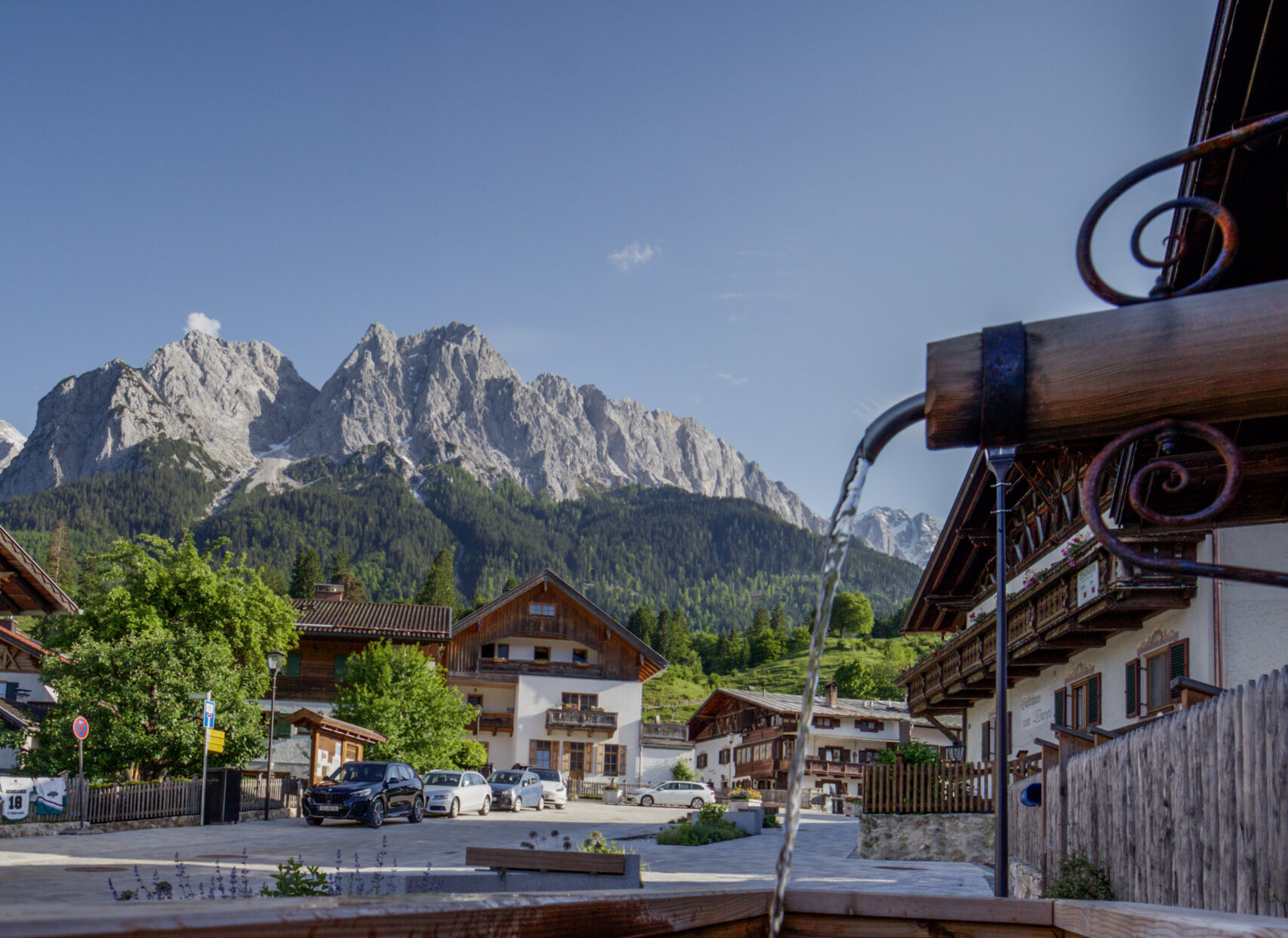 Oberer Dorfplatz in Grainau im Hintergrund Waxensteine und Zugspitze mit Brunnen im Vordergrund
