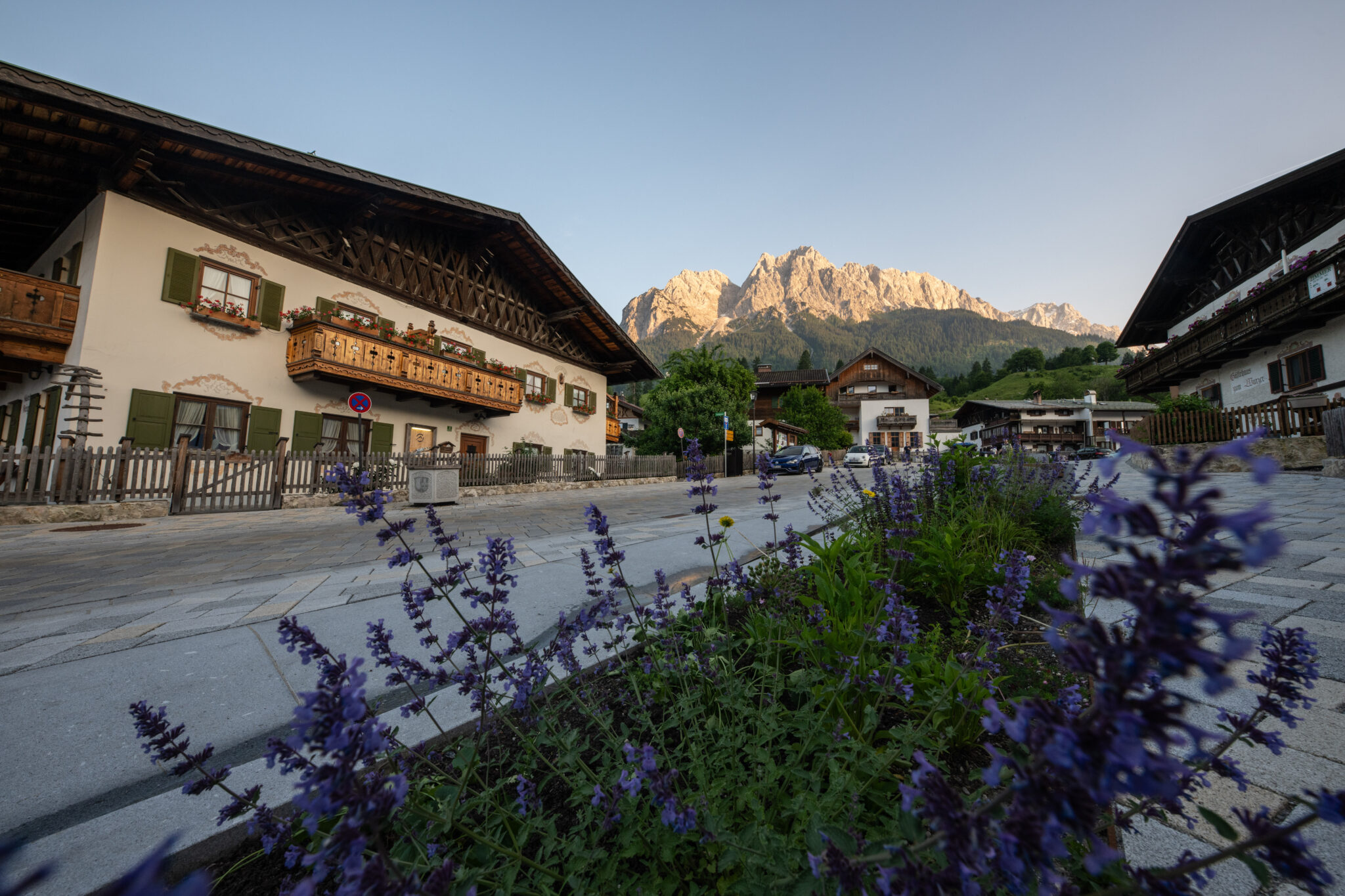 Obergrainauer Dorfplatz mit lila Blumjen im Vordergrund im Hintergrund Berge
