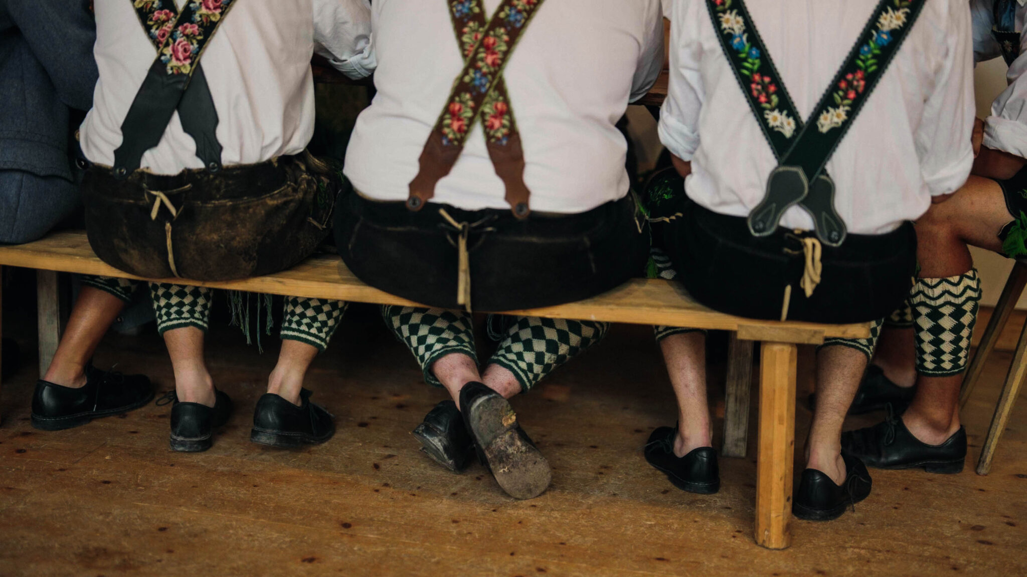 Männer in Lederhosen auf Bank von hinten forografiert