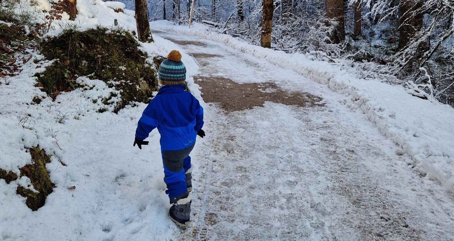 kleines Kind im Schneeanzug auf verschneiten Wanderweg